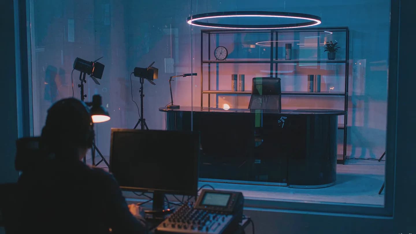 A live commerce studio at night with an empty host desk, ring light and product shelf, and an operator working at a mixing console in the foreground
